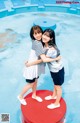 A couple of young women standing next to each other near a pool.