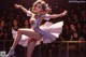 A woman in a white dress dancing in front of a crowd.