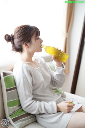 A woman sitting on a couch drinking from a bottle.