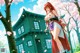A woman with long red hair stands in front of a traditional green house under a cherry blossom tree.