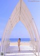 A woman in a white bikini standing in front of a white archway.