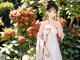 A woman in a white kimono standing in front of a bush of flowers.